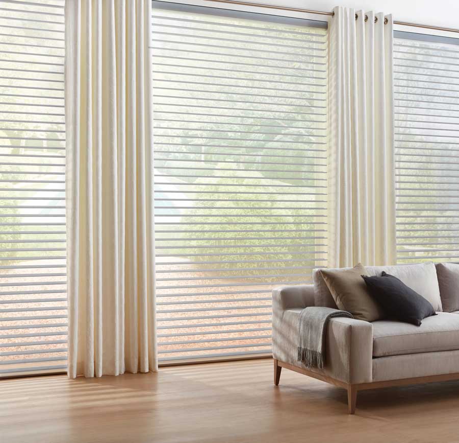 living room with floor to ceiling windows, covered with sheer shades and cream curtains