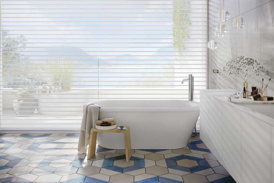 primary bathroom with sheer shades on the ceiling height windows and blue tile flooring