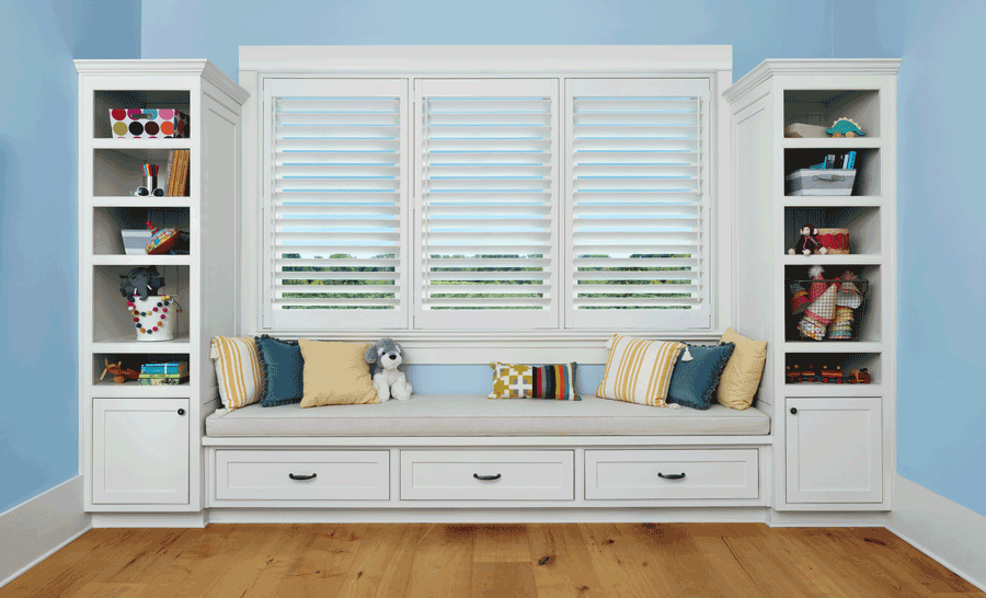 white shutters on three windows in between bookshelves over fabric bench