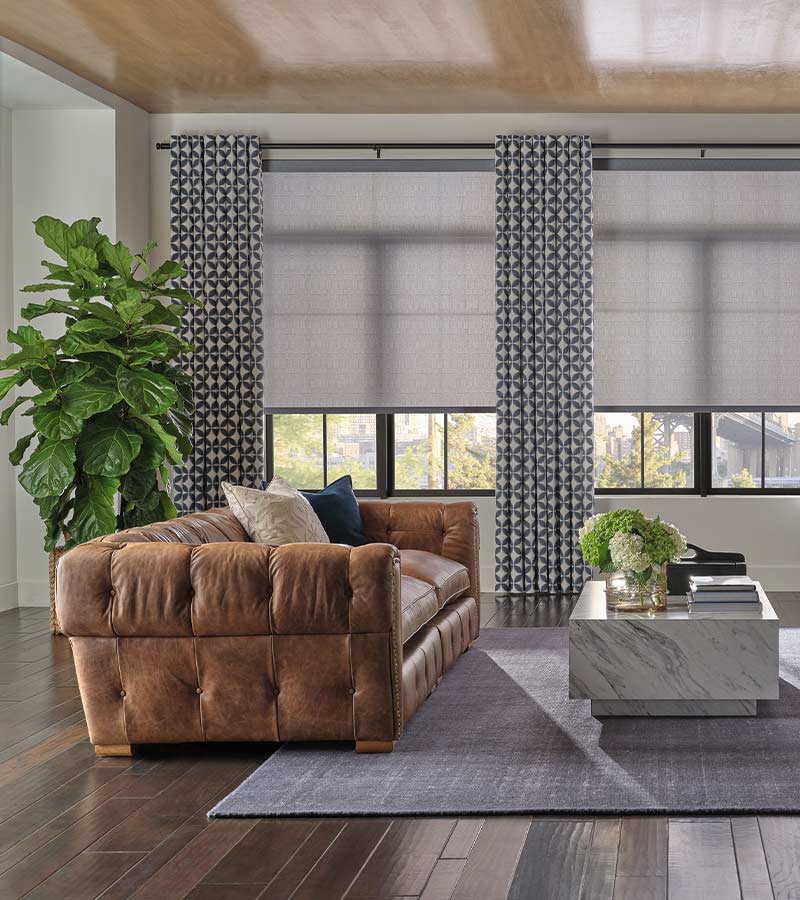 drapery and roller shades livingroom with blue and neutral colors and brown leather couch